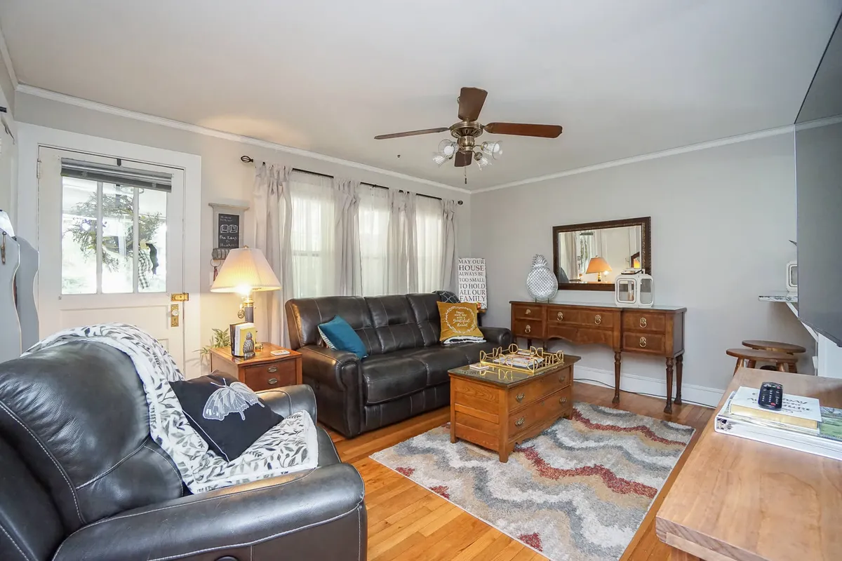 A cozy farmhouse-style living room features plush leather sofas, a wooden coffee table, and large windows dressed with curtains. The space feels warm and inviting, suggesting a gathering place for families to share stories, relax after adventures, and enjoy modern comforts amid nostalgic touches.