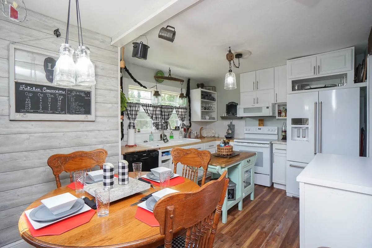 Featuring a cozy dining table and kitchen island beneath stylish hanging lights, this image offers a clear view of a welcoming space designed for family meals and group gatherings. A blackboard menu on the wall adds to the rustic yet contemporary charm, underscoring the theme of sharing recipes and memories.