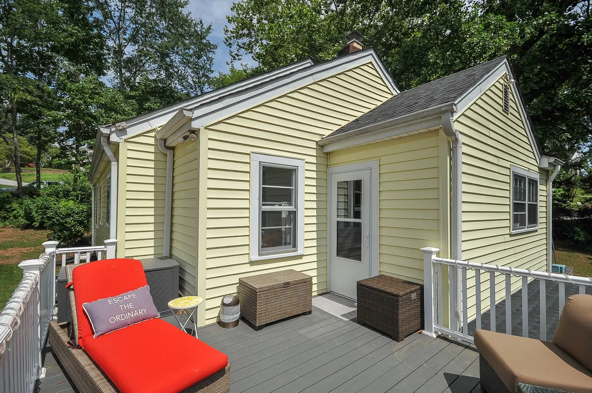 Features the yellow exterior of the house with cozy red outdoor seating and a white railing, creating a comfortable spot for relaxing and connecting with nature. The porch is bathed in warm light, suggesting moments of quiet reflection or casual conversation after a day in town.