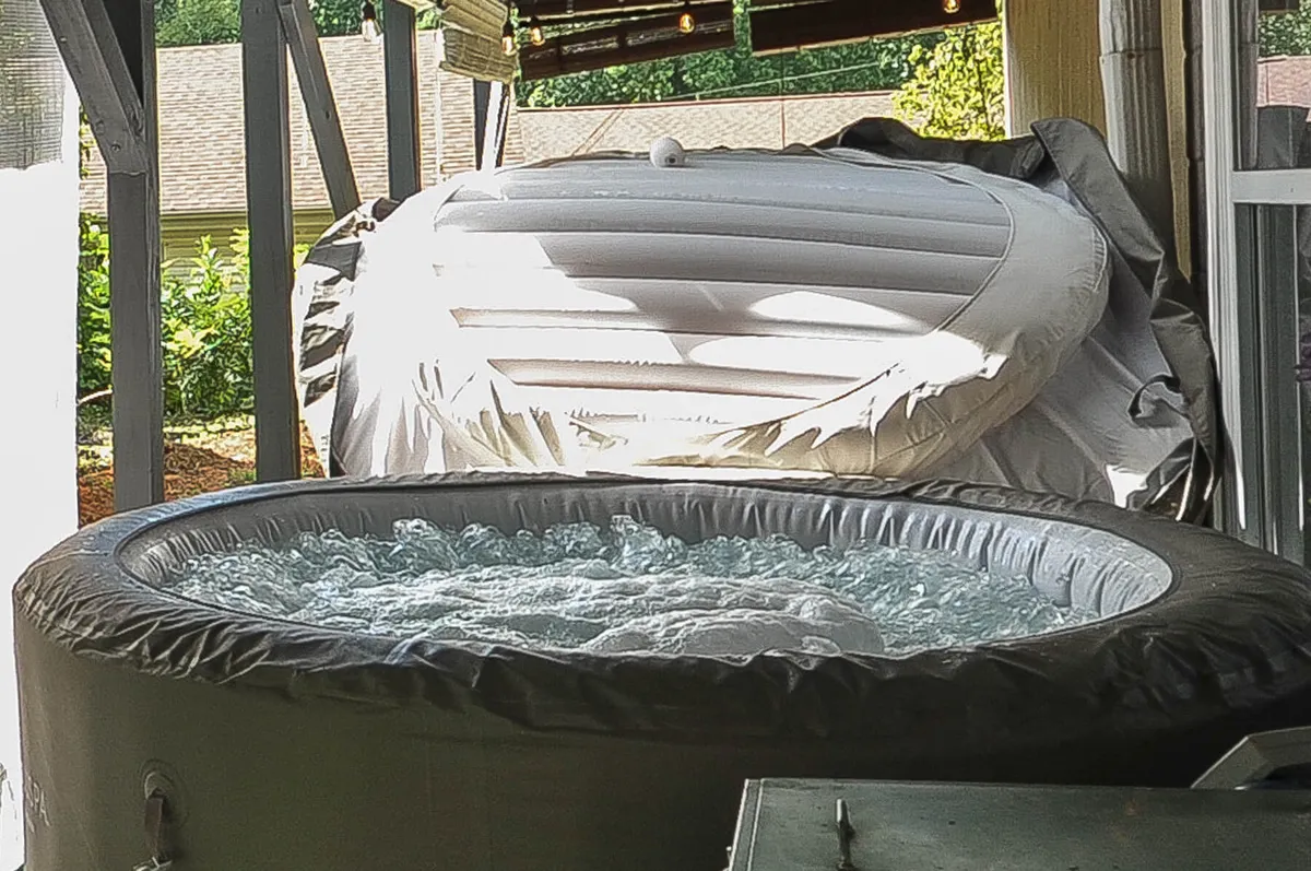 This image features an inflatable hot tub nestled on a deck, surrounded by lush greenery. The hot tub is the clear focal point, offering a serene place to relax while being immersed in nature. The setting suggests privacy and tranquility, with the inviting deck area blending seamlessly into the natural landscape.