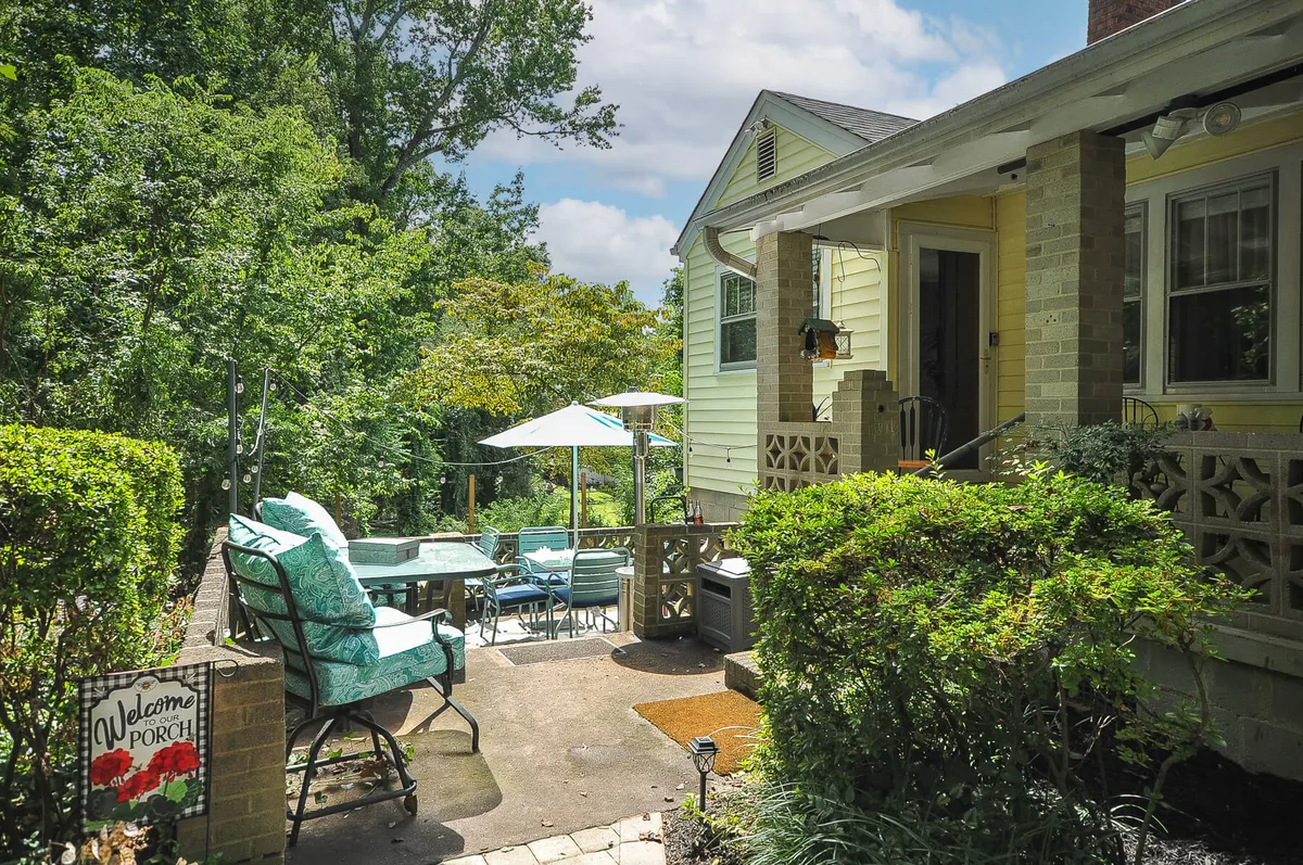 The image shows the exterior of the property, featuring a welcoming porch with comfortable furniture, a visible welcome sign, a patio area, and a glimpse of the pool area in the background. The soft lighting hints at sunset, creating a cozy and inviting outdoor atmosphere ideal for relaxing after a day out.