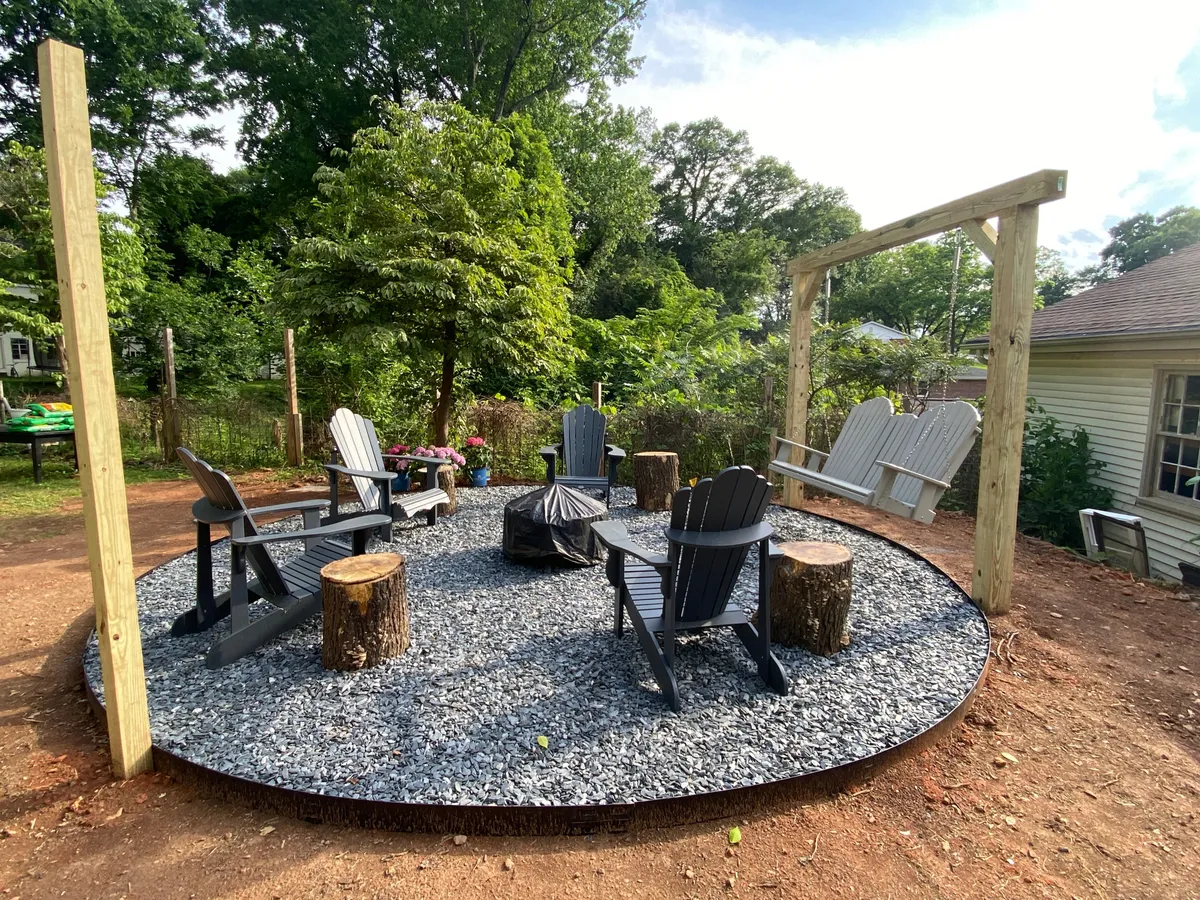 This image features a communal outdoor fire pit area surrounded by Adirondack chairs, a swing set, and stump seats, all set in a relaxed gravel circle under open skies. The setting is perfect for gathering, stargazing, and unwinding as the day ends.