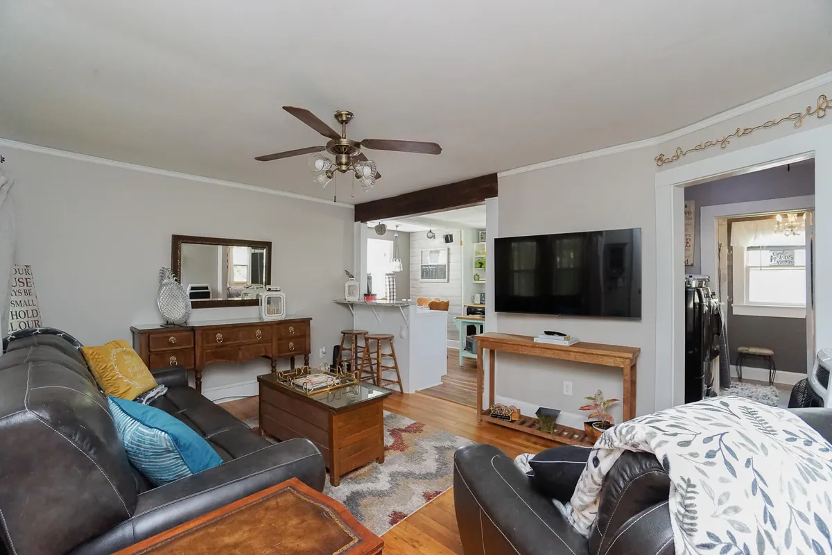 A living room with a leather sofa, a wooden coffee table, a wall-mounted TV for entertainment, and a decorative mirror. The space is arranged for relaxing with family or friends, combining antique-style elements with modern amenities. Lighting is soft and inviting.