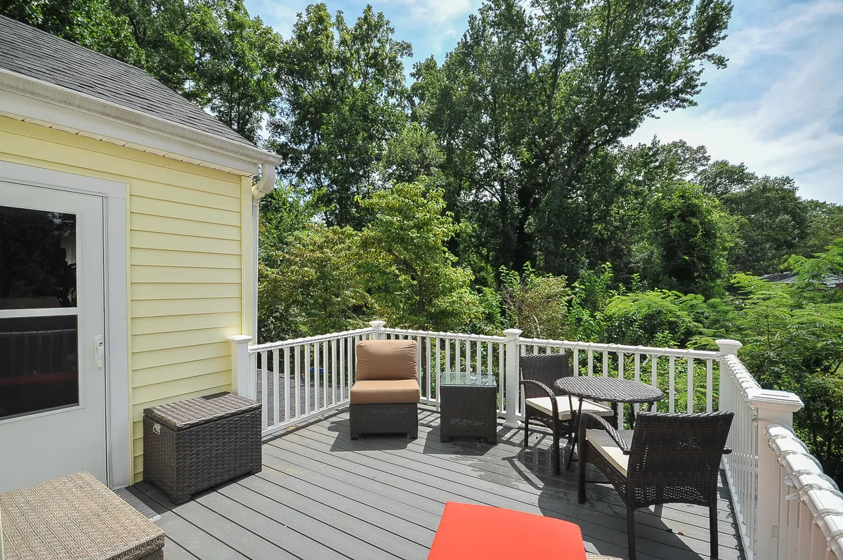 A tranquil deck furnished with comfortable seating overlooks the greenery surrounding the yellow cottage. The setting conveys peaceful mornings or afternoons spent lounging, enjoying coffee, or gathering before heading out to explore. The lush backdrop and inviting arrangement make it perfect for family bonding.
