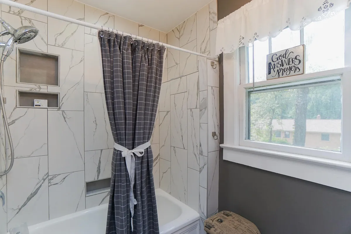 A calming bathroom featuring a bathtub with a shower curtain, a window with a decorative sign, and a soothing ambiance. The scene suggests both opportunities for relaxing soaks and quick refreshes.