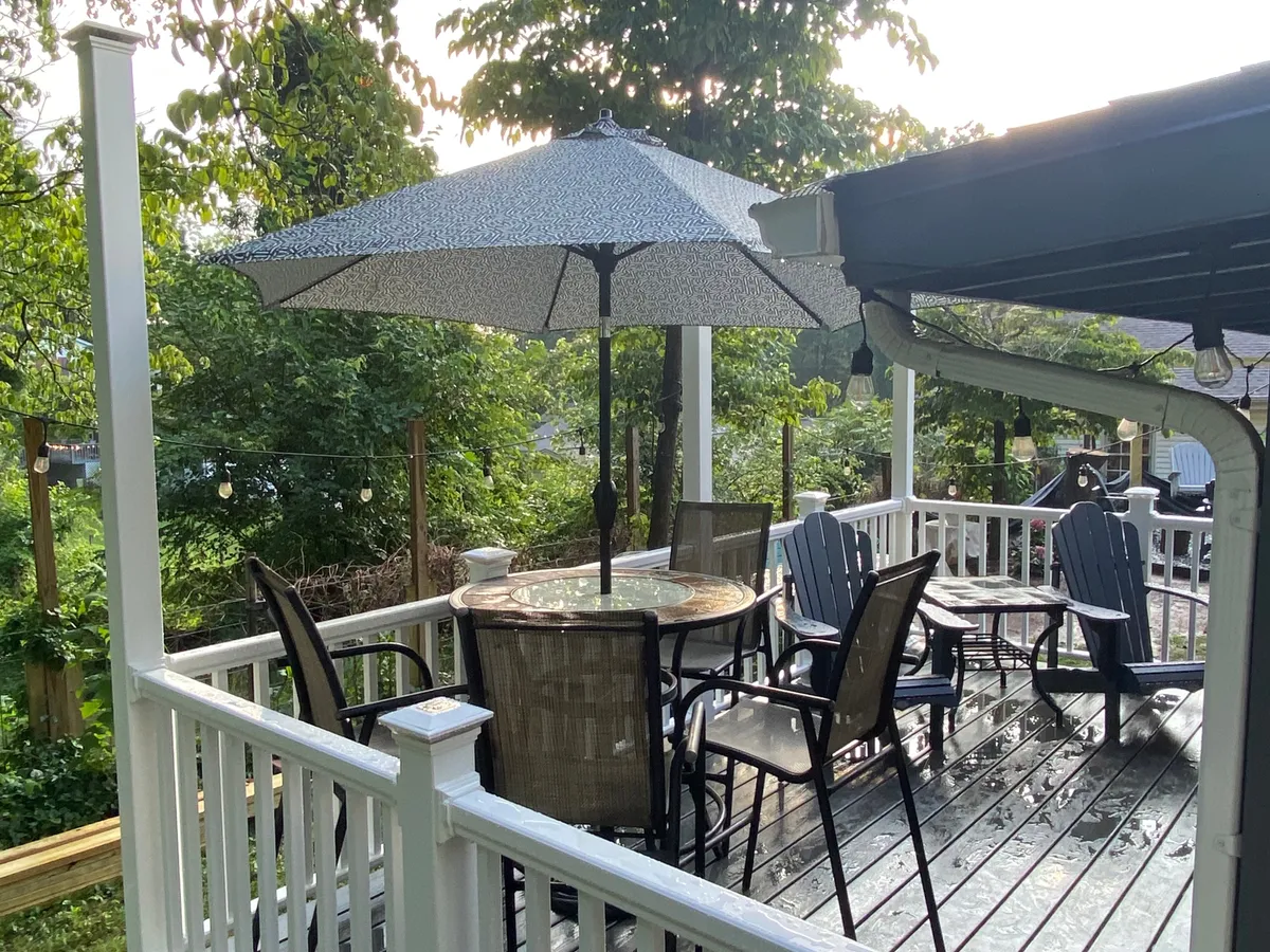 A peaceful deck scene with an umbrella-shaded table, surrounding greenery, and comfortable deck chairs. The tranquil setting suggests opportunities for al fresco dining, morning coffee, or intimate evening chats in a cozy, private environment.